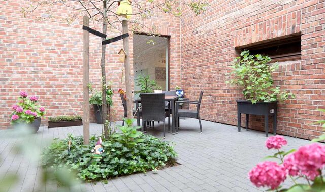 Begrünter Innenhof mit einem Gartentisch und einigen Stühlen. 
