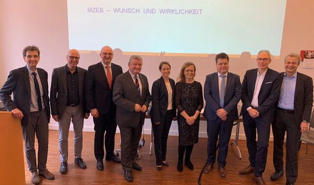 Einige Herren und zwei Damen auf einer Fläche vor einer Präsentation, welche an die Wand geworfen wird.