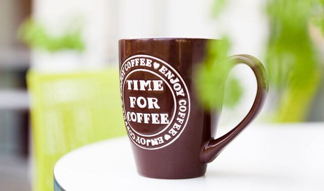 Eine Kaffeetasse auf einem Tisch. Auf der Tasse steht: Time for coffee - enjoy coffee.