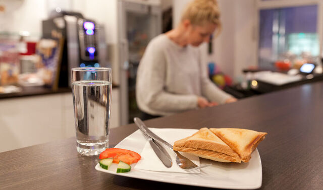 Bartresen des Café jedermann. Auf diesem steht ein Glas Wasser und ein Toastbrot. Im Hintergrund befindet sich eine Servicekraft. 